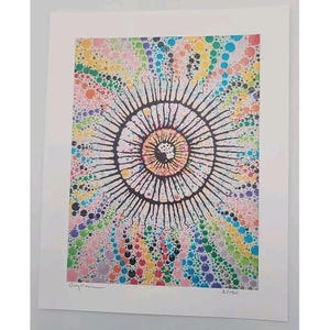May include: A colorful abstract art print featuring a central eye-like design with radiating lines. The artwork is surrounded by a vibrant array of multicolored dots, creating a dynamic and eye-catching composition. The print is numbered 2/150.