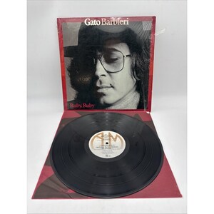 May include: A Gato Barbieri Ruby, Ruby vinyl record album with a black and white cover featuring a portrait of a person wearing glasses. The record is black with a white center label displaying the A&M Records logo and track listings.