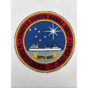 May include: A circular embroidered patch featuring a blue center with a white ship silhouette, a white starburst, and small white stars. A red border contains the black text UNITED STATES NAVAL SHIP VANGUARD (T-AG-194). A yellow banner displays SSPO-MSC.