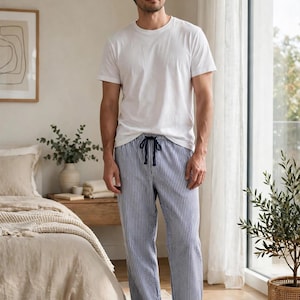 May include: A plain white short-sleeved crew neck t-shirt paired with blue and white vertical striped pajama pants featuring a dark blue drawstring waistband. The pants have a relaxed fit and a textured fabric appearance.