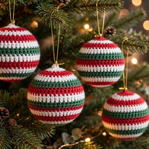 May include: Four spherical Christmas ornaments made of crocheted yarn featuring horizontal stripes in red, white, and dark green. Each ornament is suspended by a thin gold string and displays a consistent textured stitch pattern.