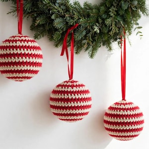 Three handmade crocheted Christmas ball ornaments in classic red and cream stripes hanging from red ribbons