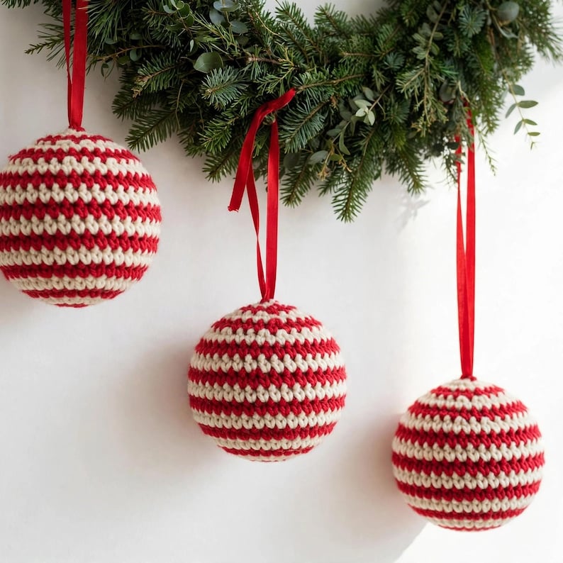 Three handmade crocheted Christmas ball ornaments in classic red and cream stripes hanging from red ribbons