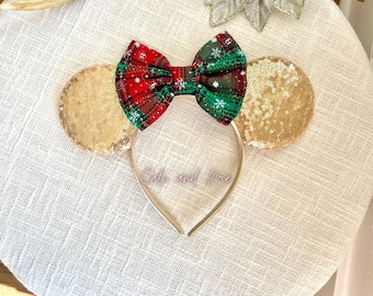 May include: A festive headband with a plaid bow in red, green, and white, adorned with snowflake accents. The headband features gold sequined ears and a clear plastic band with the text "Cole and Mae".