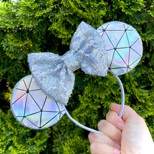 May include: A pair of silver glitter mouse ears with a large silver bow and iridescent geometric patterned ears.