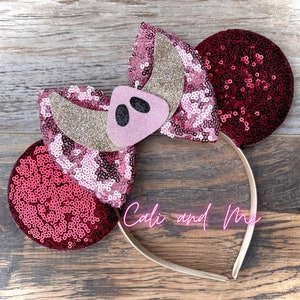 May include: Red and pink sequined Minnie Mouse ears with a pink pig snout and black eyes on the bow. The headband is gold.