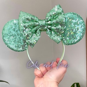 May include: Mint green sequin Minnie Mouse ears headband with a large bow. The headband is made of a soft, flexible material and is perfect for any Disney fan.