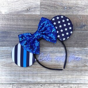 May include: Blue and white mouse ears with a blue sequin bow. The ears feature a thin blue line and a white star pattern.
