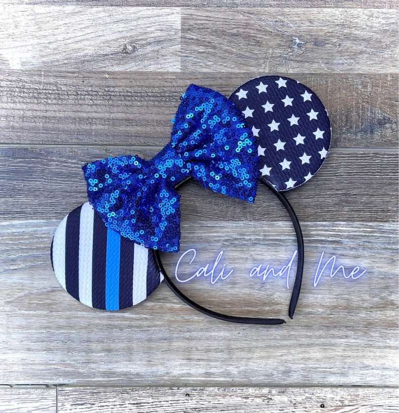 May include: Blue and white mouse ears with a blue sequin bow. The ears feature a thin blue line and a white star pattern.