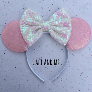 May include: Pink and white sequined Minnie Mouse ears headband with a white bow and the text "Cali and Me" on the headband.