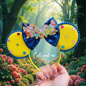 May include: Yellow and blue sequined mouse ears headband with a bow featuring a cartoon image of the Seven Dwarfs. The headband has colorful gems and the text "Cali and me".
