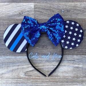 May include: Blue and black mouse ears with a blue sequin bow. The ears feature a thin blue line and a white star pattern.