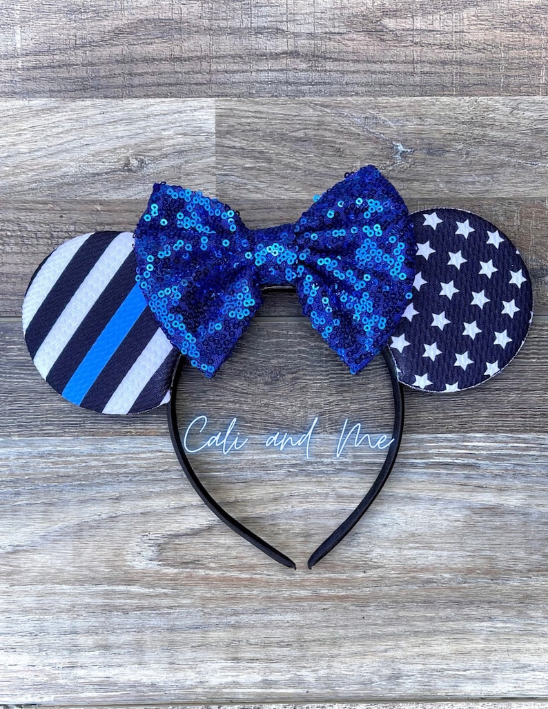 May include: Blue and black mouse ears with a blue sequin bow. The ears feature a thin blue line and a white star pattern.