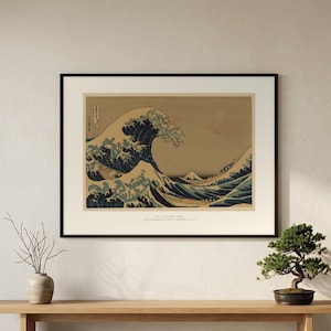 Hokusai's Great Wave in a black frame on a wall above a wooden bench with a bonsai