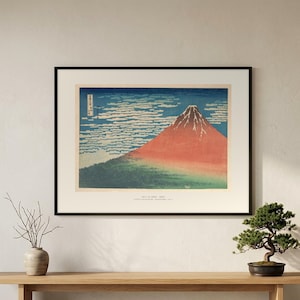 Hokusai's Red Fuji in a black frame on a wall above a wooden bench with a bonsai