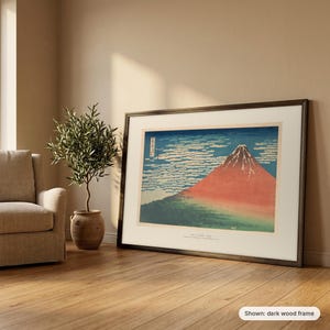 Hokusai's Red Fuji in a dark wood frame leaning against a wall beside an armchair and an olive tree