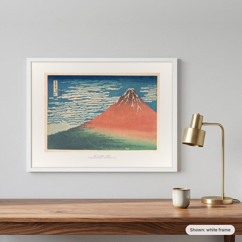Hokusai's Red Fuji in a white frame on a grey wall beside a brass lamp
