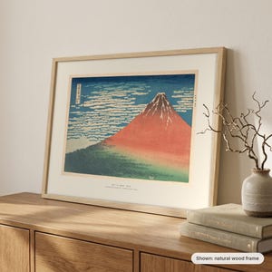 Hokusai's Red Fuji in a natural wood frame leaning on a sideboard beside a vase of branches