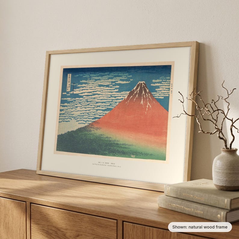 Hokusai's Red Fuji in a natural wood frame leaning on a sideboard beside a vase of branches