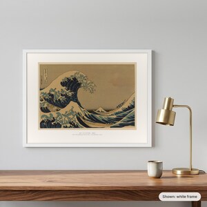 Hokusai's Great Wave in a white frame on a grey wall beside a brass lamp