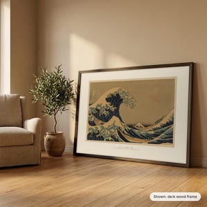 Hokusai's Great Wave in a dark wood frame leaning against a wall beside an armchair and an olive tree