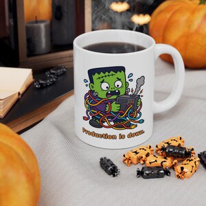 May include: A white ceramic mug featuring a cartoon illustration of a green Frankenstein-style monster tangled in colorful electrical cords while holding a smoking computer server. The text below the graphic reads, "Production is down."