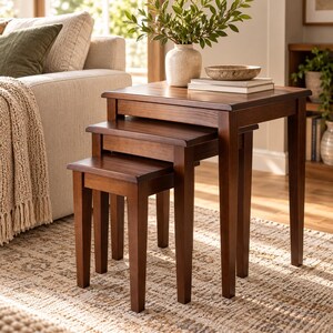 May include: A set of three nesting tables crafted from dark brown wood, featuring square tops and straight legs. The tables are arranged in a descending height order, with the largest table supporting a ceramic vase and books.