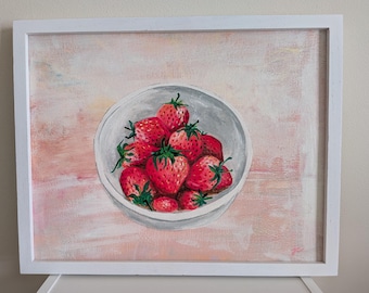 May include: A framed painting featuring a white bowl filled with bright red strawberries with green stems. The background is a soft, textured blend of light pink and peach tones, creating a gentle contrast with the vibrant fruit.