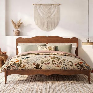 May include: A wooden bed frame with a curved headboard featuring a woven cane insert. The bed is dressed in a cream-colored duvet cover decorated with a colorful botanical and butterfly print, paired with solid sage green and patterned pillows.