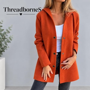 May include: An orange hooded jacket with a front button closure, worn over a white top and dark gray jeans. The text ThreadborneS with a heart icon is visible in the upper left corner of the image.