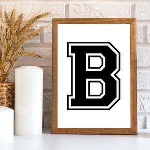 May include: A black and white letter B in a varsity style font. The letter is framed in a brown wood frame.