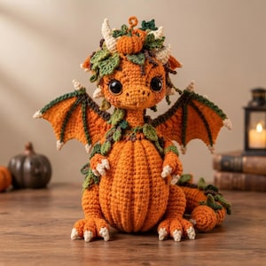May include: A crocheted dragon plush toy with a body shaped like a pumpkin. The creature features orange yarn, green leaf accents, small horns, and large dark eyes. It has outstretched wings, clawed feet, and a tail, all crafted with detailed stitching.