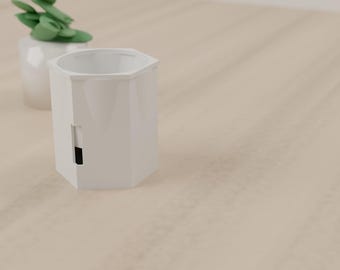 May include: A white hexagonal planter with a small rectangular cutout near the base revealing a dark interior. A small green succulent plant in a white pot is positioned slightly behind and to the left of the main hexagonal planter.