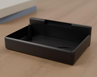 May include: A matte black rectangular tray with a low-profile back wall and a single vertical peg positioned in the left corner. The tray features a smooth, solid construction with rounded edges and a recessed circular indentation on the base.