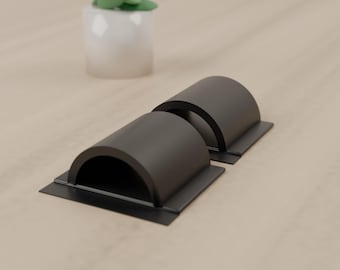 May include: Two matte black metal cable management organizers featuring a semi-cylindrical arch design with a flat rectangular base. These hardware components are designed to secure and route cables along a flat surface.
