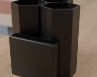 May include: A matte black desk organizer featuring two tall hexagonal compartments and one shorter rectangular compartment attached to the front, providing multiple sections for storing pens, pencils, or other small office supplies.