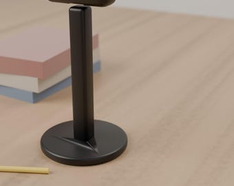 May include: A matte black headphone stand featuring a vertical post, a circular base, and a horizontal top bar designed to hold headphones. The stand has a smooth, solid construction with a clean, functional design for desktop organization.