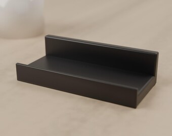 May include: A matte black rectangular display stand featuring a low front ledge and a taller back panel, designed with clean lines and a smooth finish to hold small items securely in an upright position for clear visibility.