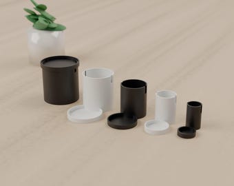 May include: A set of five cylindrical containers in varying sizes, alternating between black and white colors. Each container features a matching circular lid. A small white pot with a green succulent plant is positioned in the background.