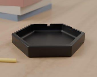 May include: A matte black hexagonal tray with a smooth, solid finish and a shallow interior basin. The tray features a geometric six-sided shape with clean, straight edges and a wide, flat rim, providing a simple and functional design.