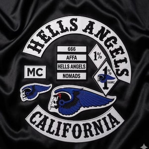 Puede incluir: Una prenda de tela negra con parches bordados que incluyen un arco blanco grande con el texto negro HELLS ANGELS, un arco más pequeño con CALIFORNIA, una calavera con alas azules, un parche de diamante con 1% y HAMC, y MC.