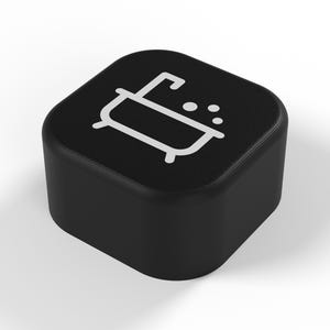 May include: A square black button with rounded corners featuring a white graphic icon of a bathtub with bubbles on the top surface. The object has a smooth matte finish and a solid construction, presenting a clear and simple visual design.