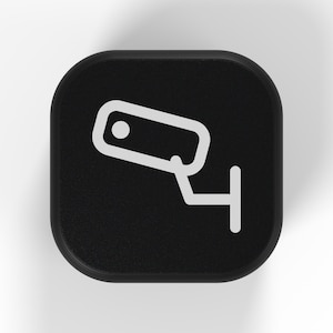 Peut inclure: Un bouton carré noir aux coins arrondis présentant une icône en ligne blanche représentant une caméra de surveillance montée sur un support mural. L'icône est centrée sur la surface noire mate, offrant une représentation visuelle claire et simple.