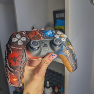 May include: A custom PlayStation 5 controller featuring a detailed graphic design. The left side displays a dark red, vine-like pattern with a silhouette, while the right side shows illustrated character portraits. The center touchpad depicts a lightning storm.