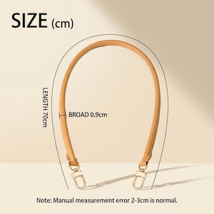 May include: A tan leather bag strap with gold-toned metal swivel clasps at both ends. The strap is arched in a U-shape. Text on the image indicates a length of 70 cm and a width of 0.9 cm. A note states that a manual measurement error of 2-3 cm is normal.
