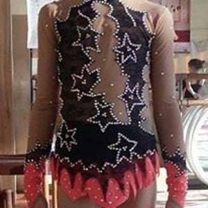 May include: A black and nude leotard with long sleeves and a star design. The leotard has a pink trim and rhinestones.