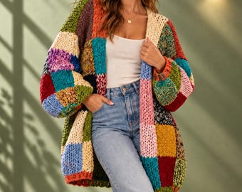 May include: A chunky knit cardigan featuring a multi-colored patchwork design with large squares in shades of red, blue, green, yellow, pink, and cream. The garment has long sleeves and an open front. The text VelmoreCrafts! WINTER WEAR is visible.