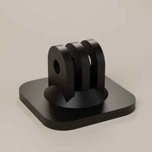 Puede incluir: Una base de montaje para cámara de color negro que presenta una placa cuadrada con esquinas redondeadas y un conector central de tres puntas. El conector tiene orificios circulares alineados horizontalmente para su fijación, con un acabado mate.