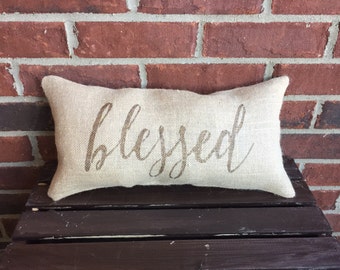 May include: A beige burlap pillow with the word "blessed" written in brown cursive lettering. The pillow is sitting on a dark brown wooden crate.