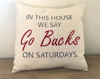 May include: A white throw pillow with the text "In this house we say Go Bucks on Saturdays." The text "Go Bucks" is in red.